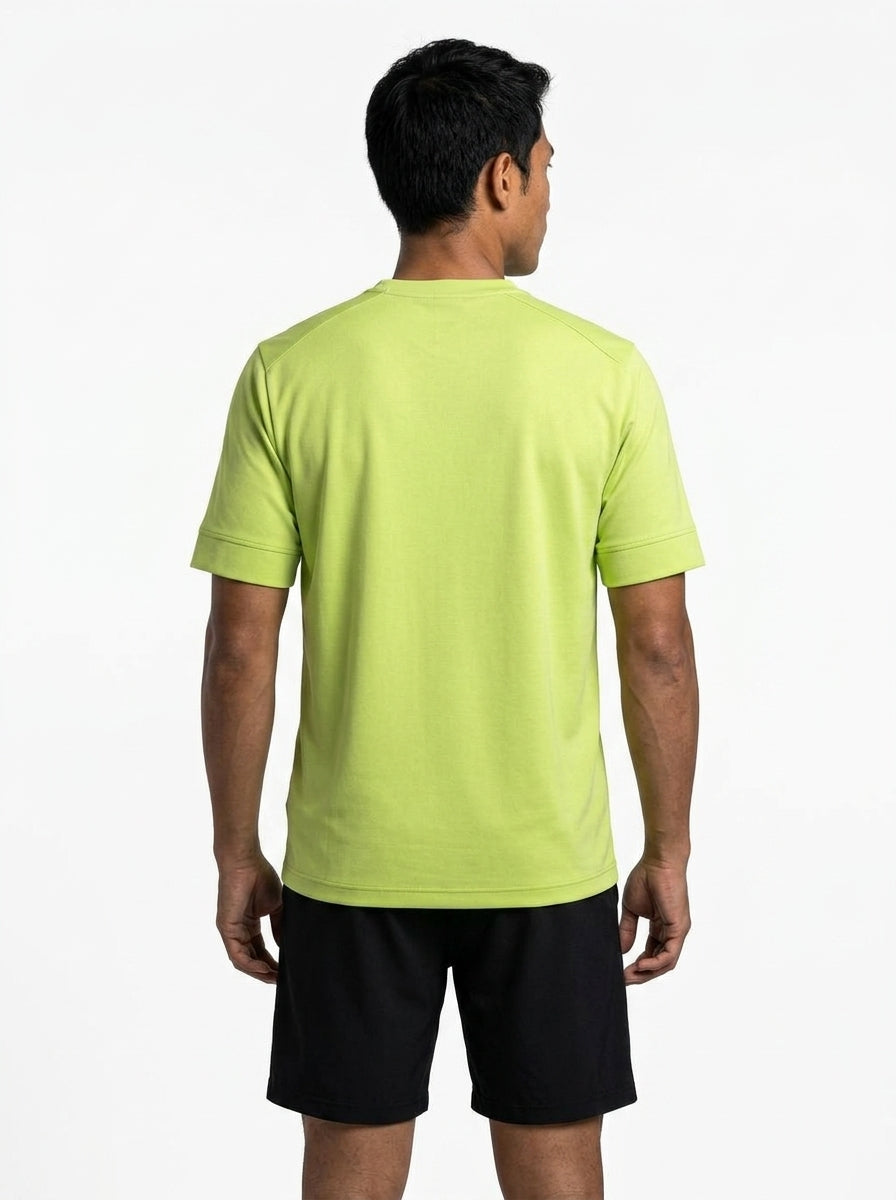 A man stands with his back to the camera, wearing a light green HEAD Slice II Mens Badminton T-Shirt by HEAD and black shorts, set against a plain white background.
