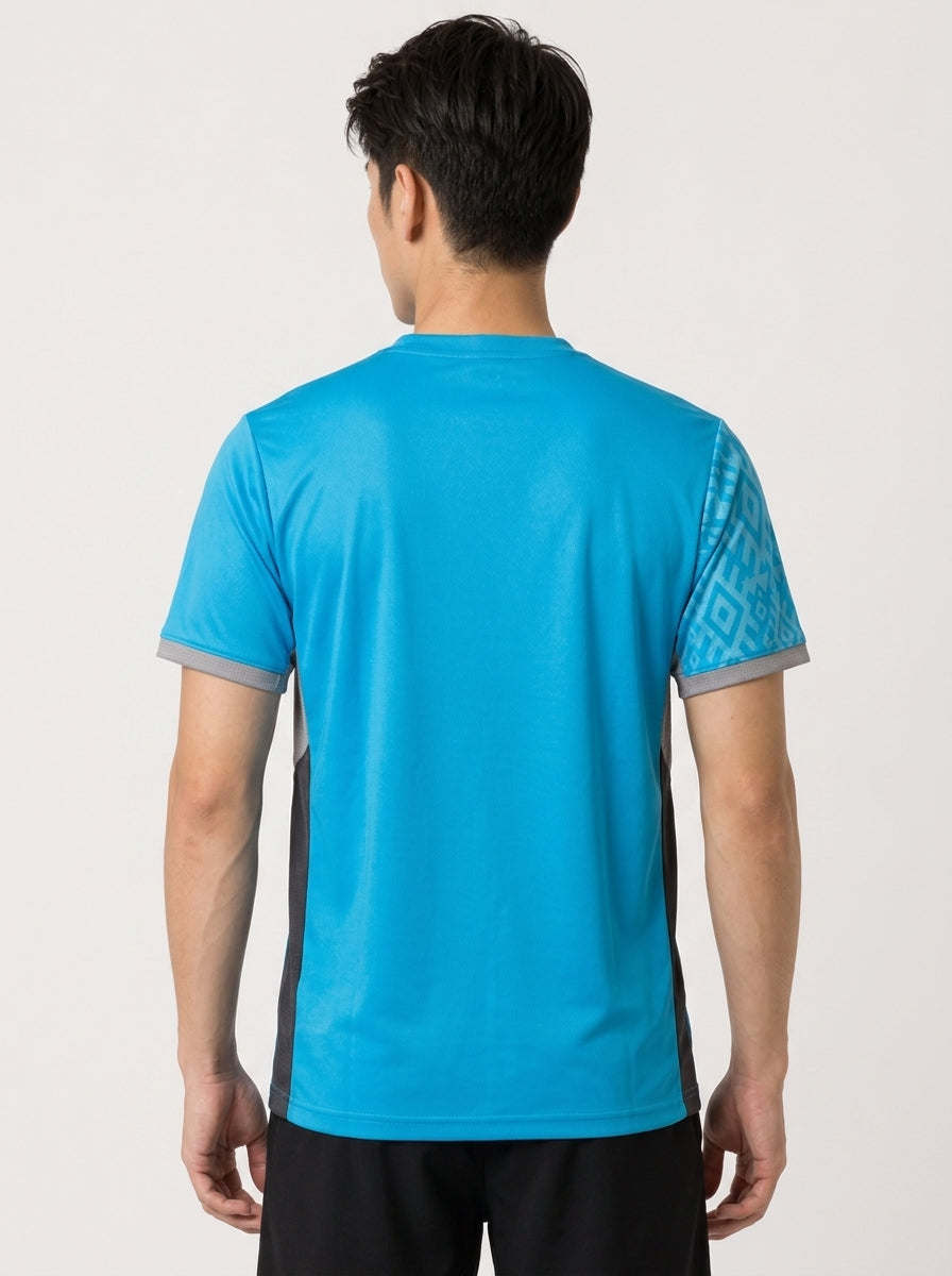 A man with short dark hair is seen from behind wearing a Yonex YTM11 Mens Badminton T-Shirt – Blue Sea with gray side panels, patterned sleeves, and black shorts against a plain light background.