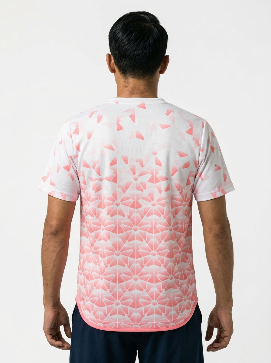 A man stands with his back to the camera, wearing the Yonex YTM2025B Men's Badminton T-Shirt in white featuring a pink geometric design, paired with dark shorts. The background is plain white.