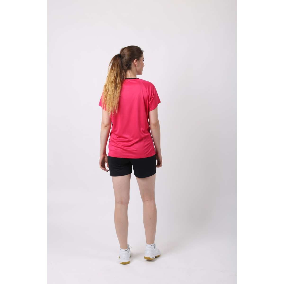 A person with long hair stands facing away, wearing the FZ Forza Blingley Sparkling Cosmo Pink Badminton T-Shirt made of quick-drying material, black shorts, and white sneakers. They are positioned against a plain white background.