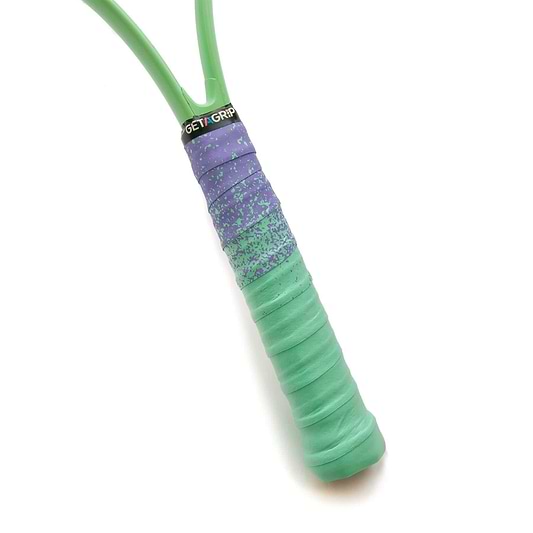 Close-up of a badminton racket handle wrapped in mint and purple overgrip tape. The top of the handle features the text "Get A Grip" on a black band, ensuring a non-slip hold with excellent moisture absorption for those intense matches.