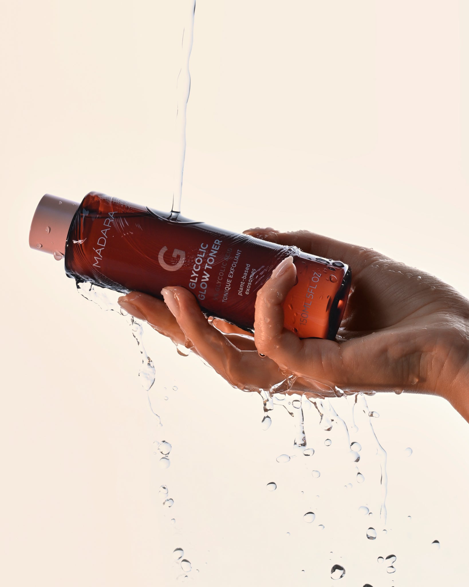 Hand holding a bottle of exfoliating MADARA Glycolic Glow Toner with water droplets around it 