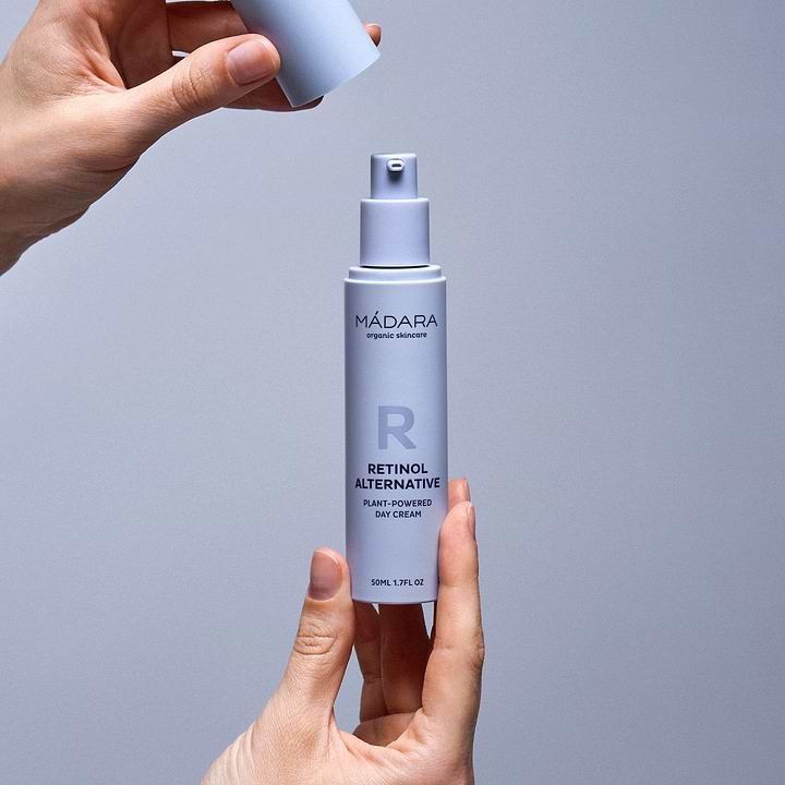 Woman holding a 50 ml pump bottle of Madara Organic Skincare Retinol Alternative Plant-Powered Day Cream with one hand and detaching the plastic cap with the other hand