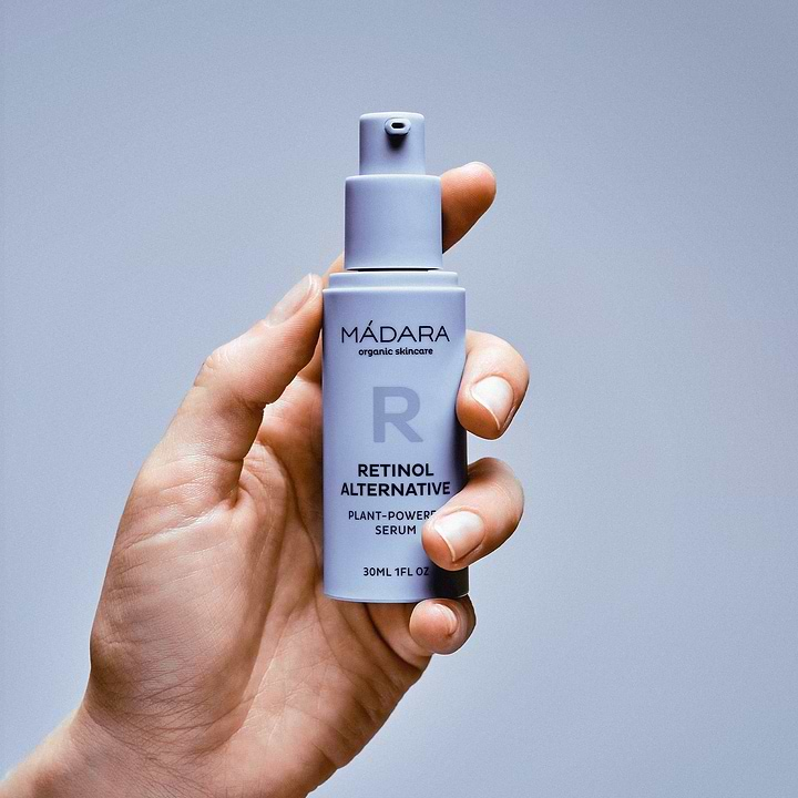 Woman's hand holding a 30ml bottle of Madara Cosmetics Retinol Alternative Plant-Powered Serum for face without a cap