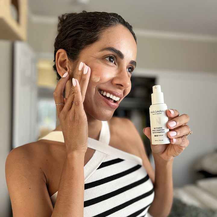 a woman holding a bottle of madara cosmetics niacinamide 5 in 1 serum in her hand and applying serum to her face