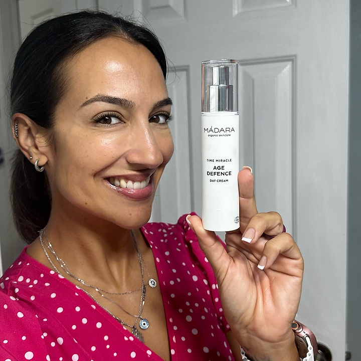 Smiling woman holding a bottle of Mádara Time Miracle Age Defence Day Cream, showcasing anti-aging skincare for a youthful glow.