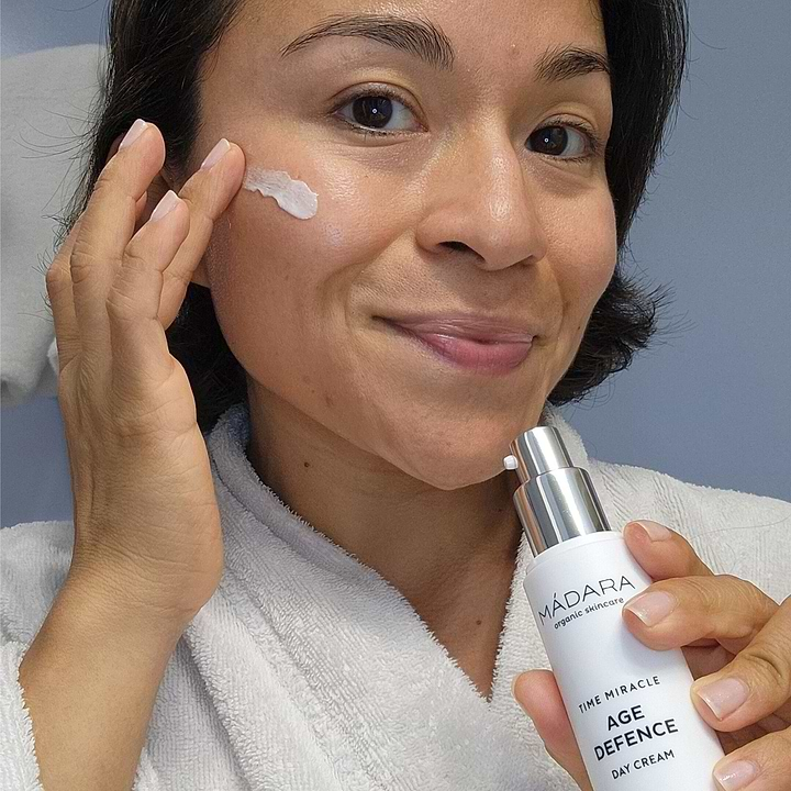 Woman applying Mádara Time Miracle Age Defence Day Cream to her face, highlighting anti-aging and skin-protective benefits for a youthful complexion.