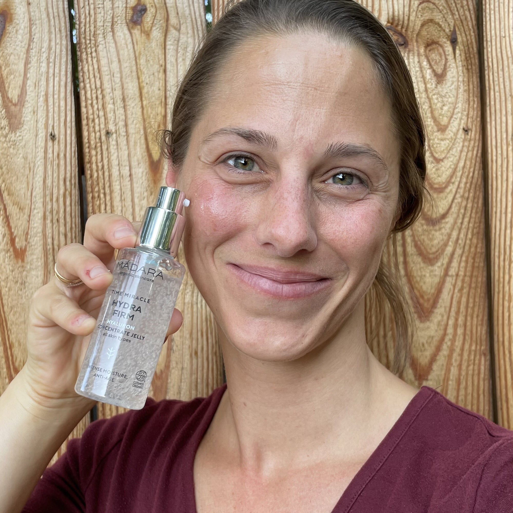 Smiling woman holding a bottle of Mádara Time Miracle Hydra Firm Hyaluron Concentrate Jelly, highlighting hydration and skin-firming benefits for a refreshed appearance.