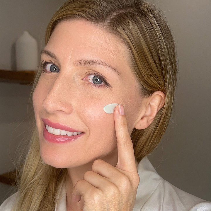 **Optimized version:**  
Smiling woman applying Mádara Cosmetics Total Renewal Night Cream to her under-eye area, highlighting hydration and anti-aging skincare benefits.