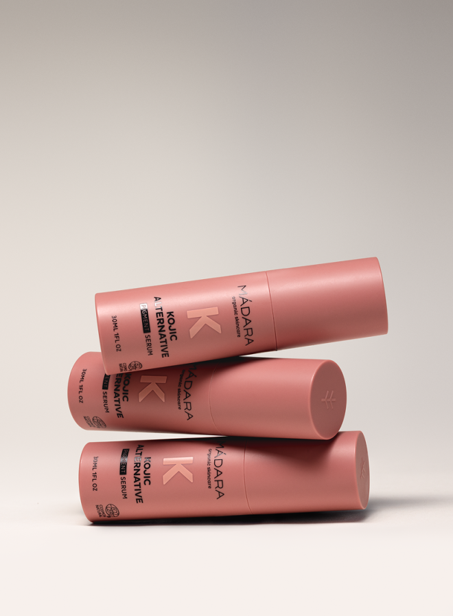 Three MÁDARA Kojic Alternative Pigment Serum bottles stacked in a balanced arrangement on a neutral background.