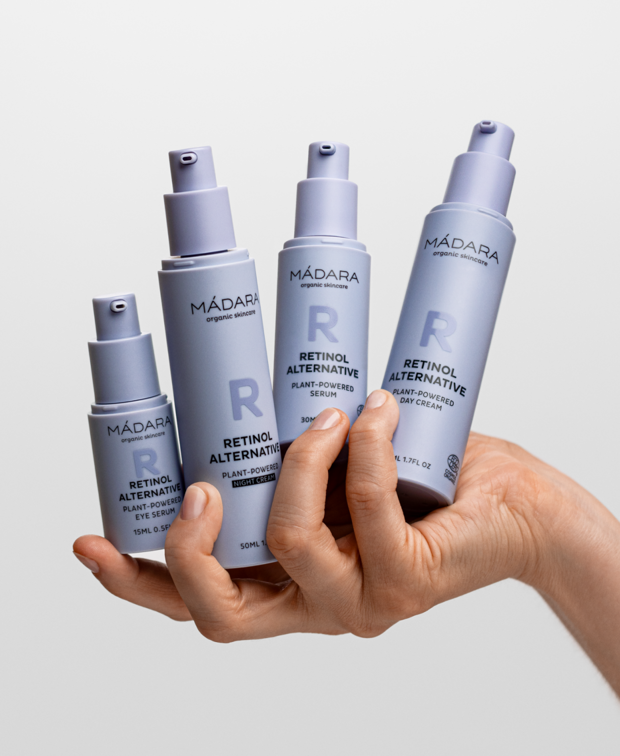 Hand holding four MÁDARA Retinol Alternative skincare products—eye serum, night cream, serum, and day cream—against a clean light background