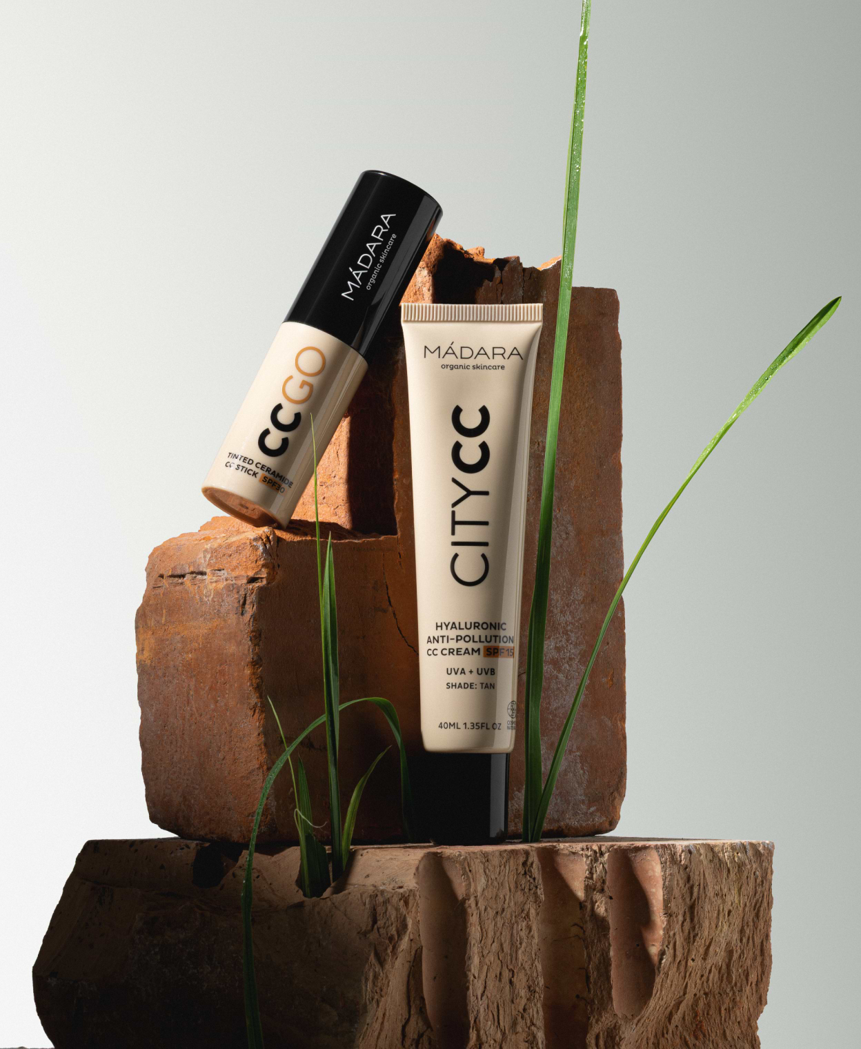 MÁDARA City CC cream and CC Go tinted stick displayed on stacked clay blocks with green grass accents against a clean background