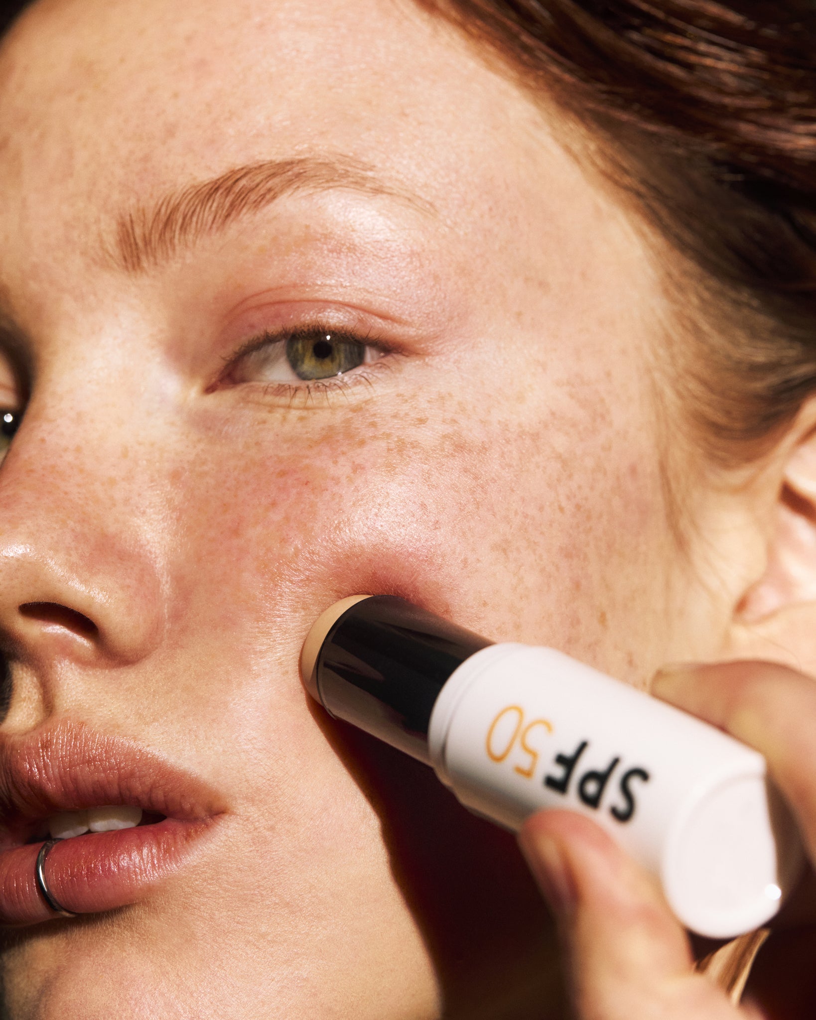 Person applying MADARA SPF 50 sunscreen stick to their face