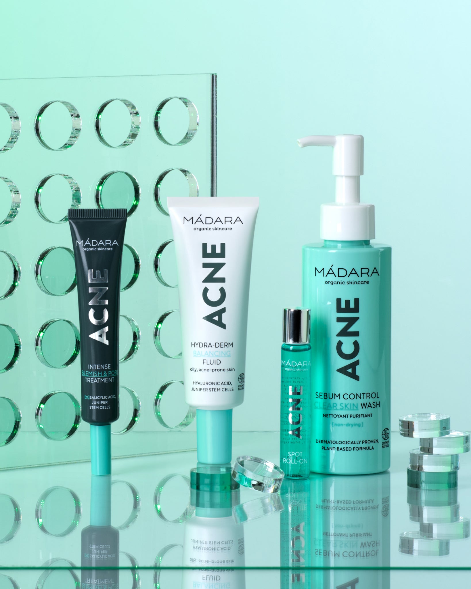 Mádara Acne skincare set products on a reflective surface with a light green background