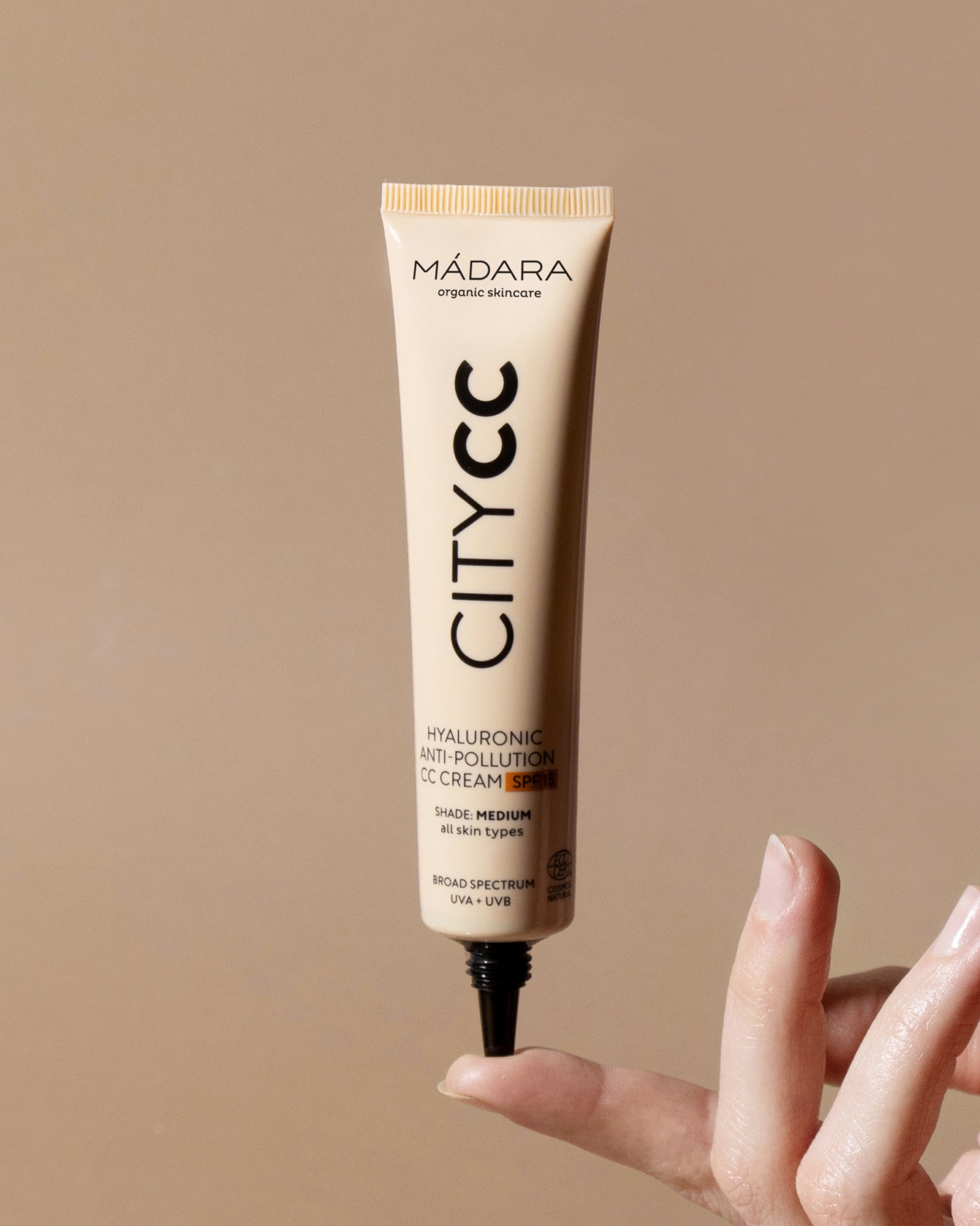 Mádara City CC cream tube held by a hand against a beige background