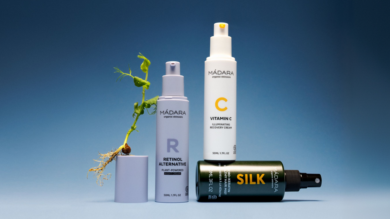 MÁDARA skincare set featuring vitamin C cream, retinol alternative and silk hair mist with sprouting plant on blue background representing renewal and glow