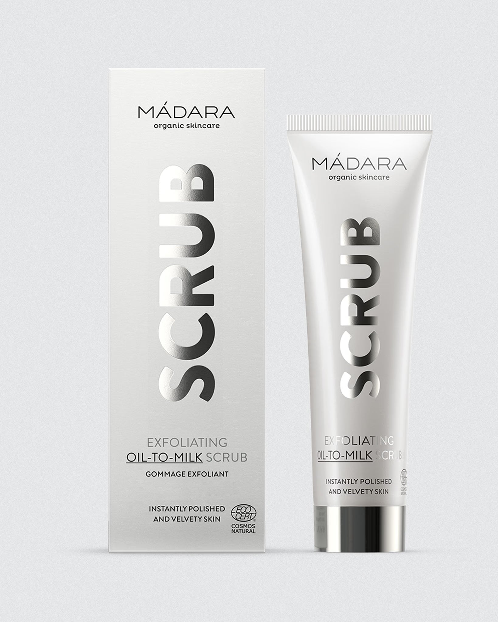 A tube of MÁDARA Exfoliating Oil-to-Milk Scrub standing next to its vertical cardboard box on a light background.