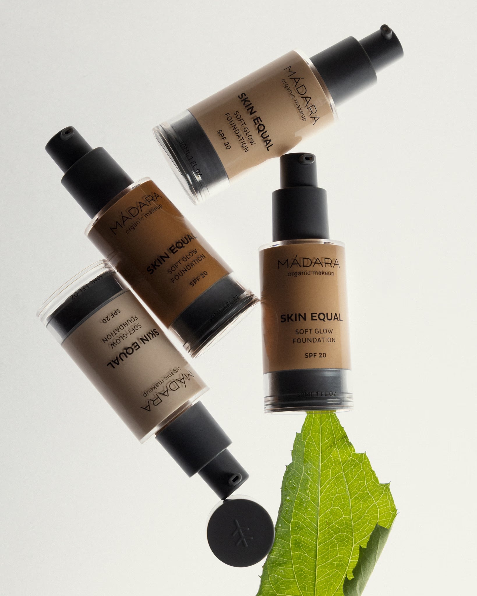 Four bottles of MÁDARA Skin Equal Soft Glow Foundation SPF 20, positioned with a leaf.
