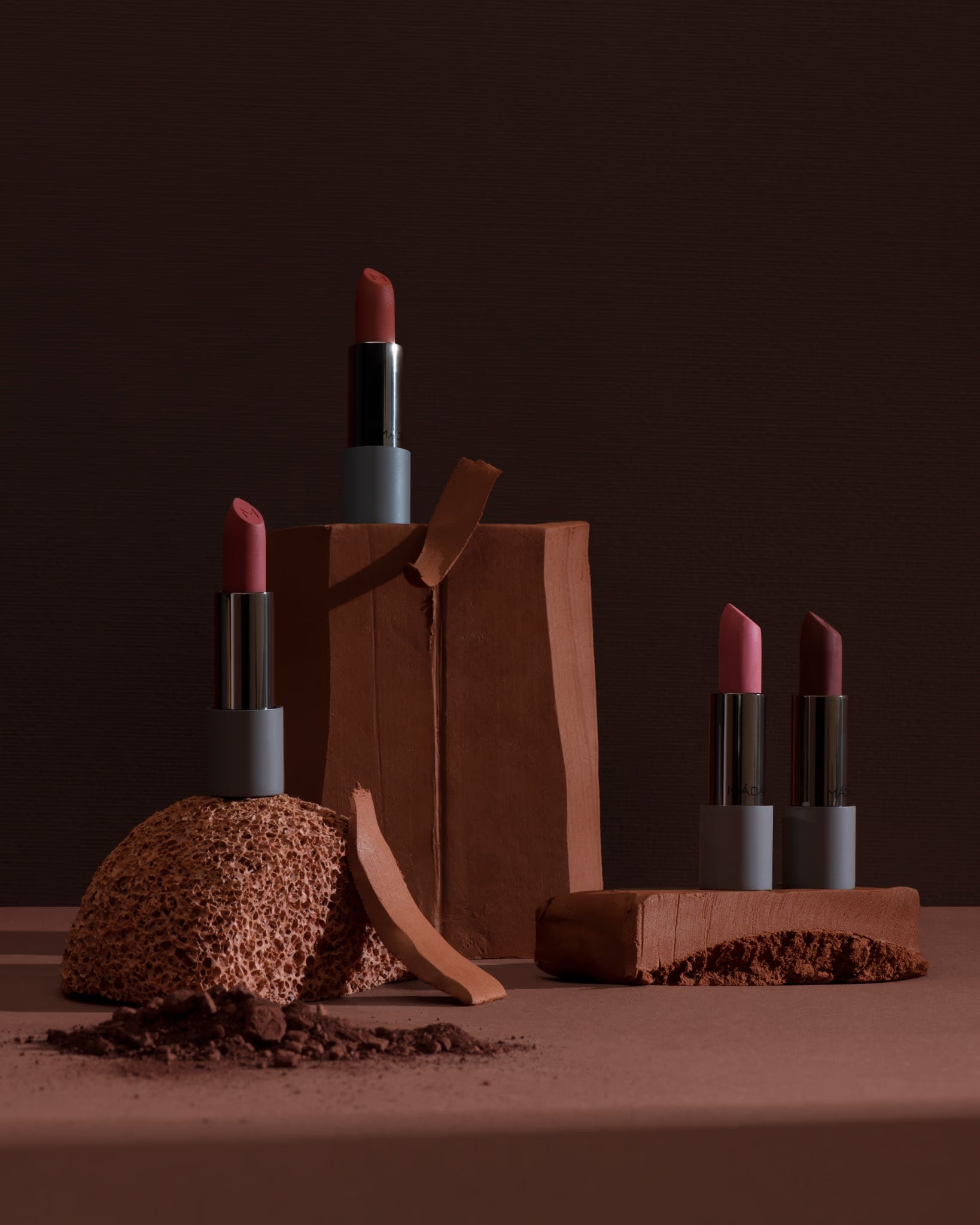 Four lipsticks arranged with clay and textured objects.