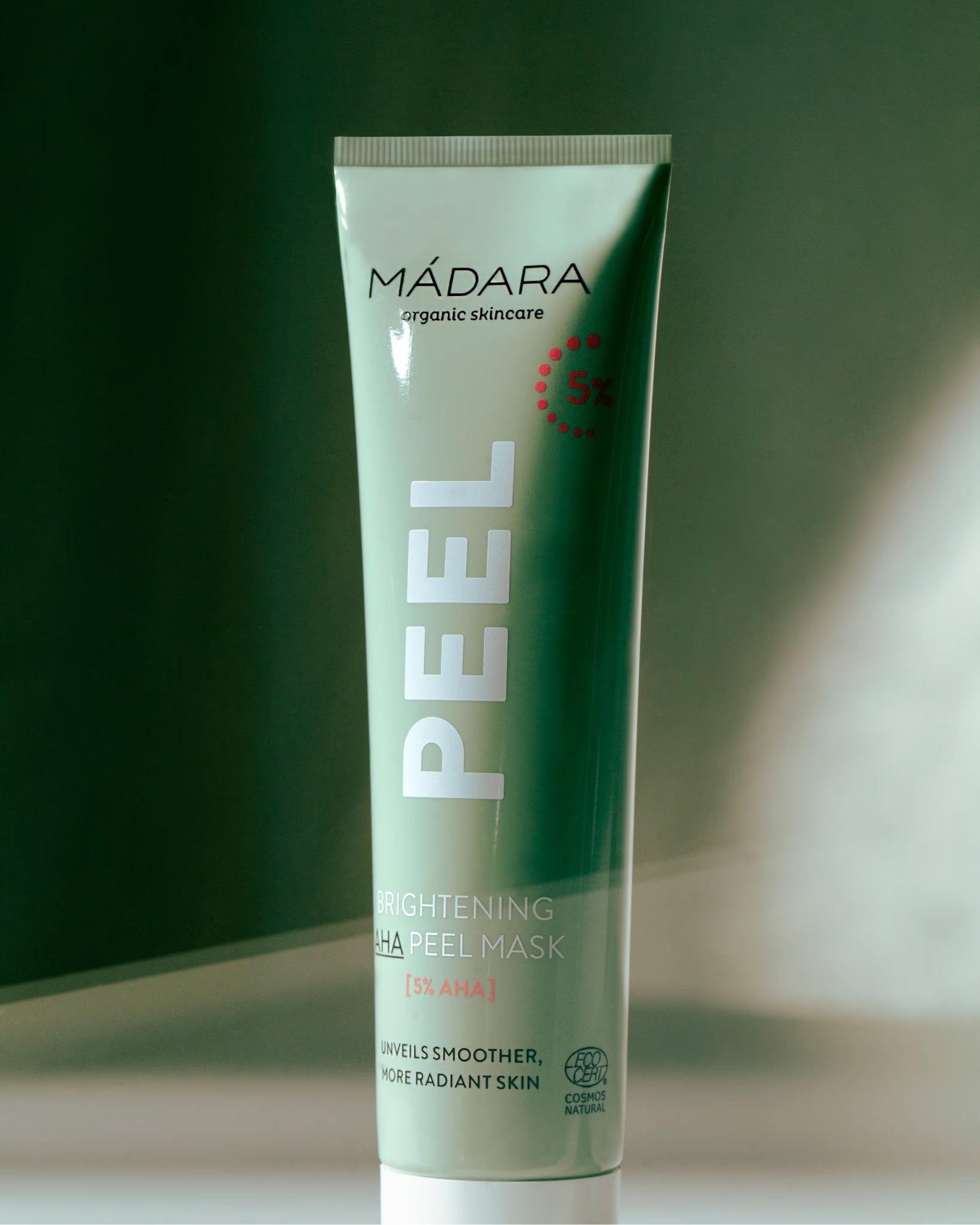 MÁDARA Brightening AHA Peel Mask against a dark green background with a ray of light.