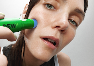 Model applying MÁDARA DEWY Hydra Caffeine Serum Stick to the chee