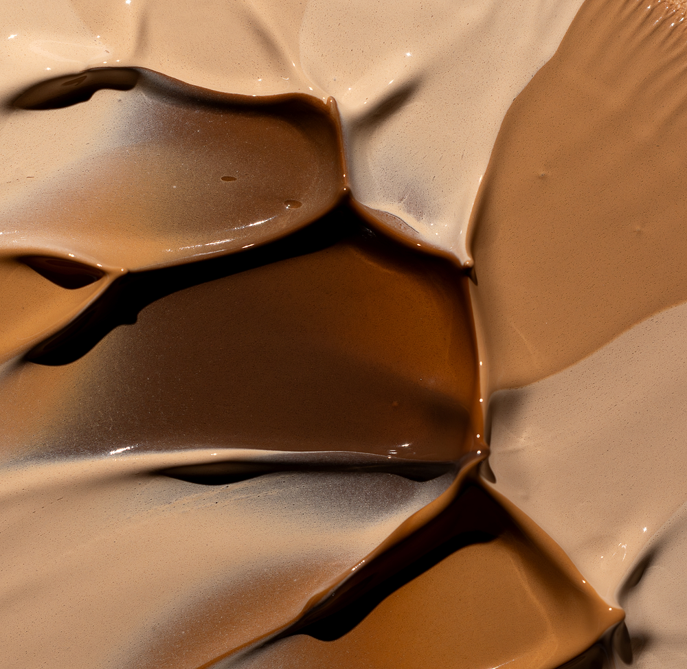 Close-up of multiple creamy foundation swatches in light to deep shades blended together with glossy, smooth texture, showcasing the shade range of MÁDARA Cosmetics Skin Equal Soft Glow Foundation SPF20
