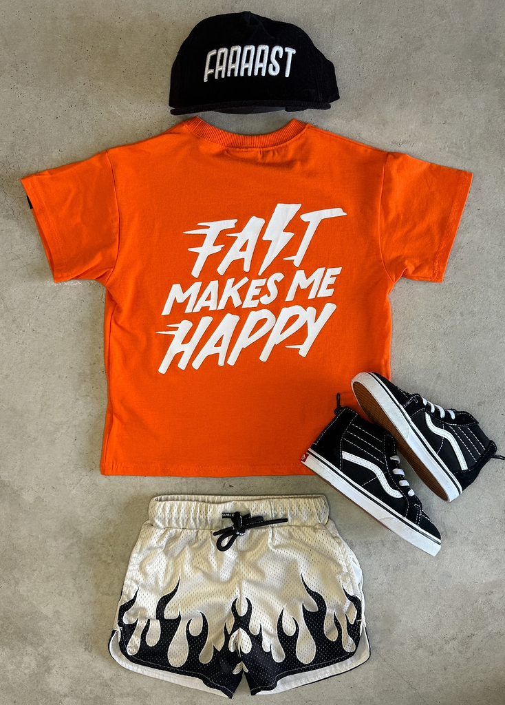 Orange t-shirt with 'Fast Makes Me Happy' text, black cap, white shorts with black flame design, and black and white sneakers on a gray surface.