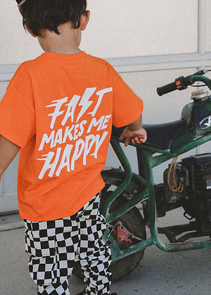 Child wearing an orange t-shirt with 'Fast Makes Me Happy' text, standing next to a green vehicle.