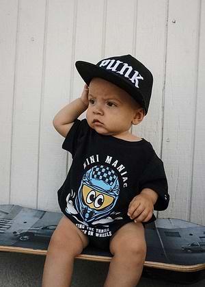Child wearing a Little Trouble black SnapBack and Mini Maniac Baby Romper sitting on a skateboard.