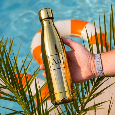 Hand holding a gold Au Vodka USA water bottle over a swimming pool with a life preserver