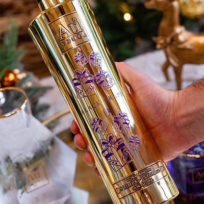 Au Vodka Black Grape Christmas Print Bottle being held in hand. Against a blurry christmas background, with a christmas tree.