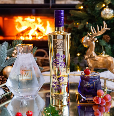 Au Vodka Christmas Bottle Black Grape 750ml and an Au Branded Glass with Purple Liquid on a blurred christmas background.