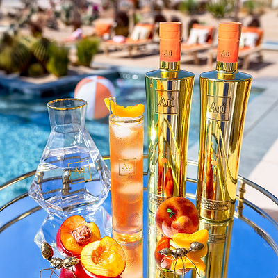 Bottle of Au Vodka Juicy Peach 750ml with a glass of vodka and peach slices in the foreground, pool in the background.