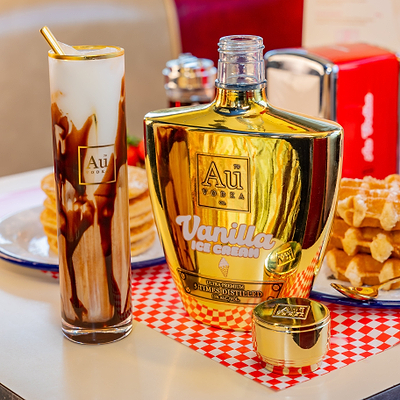 Au Vodka labeled 'Au Vanilla Ice Cream' with a Au Highrise Glass with chocolate sauce on a checkered tablecloth.