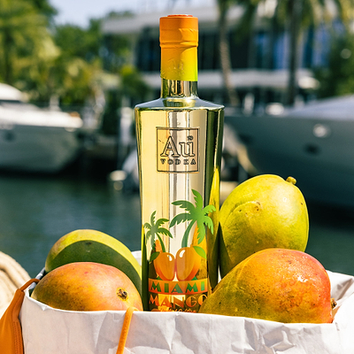 Au Vodka USA Mango Passion bottle with fresh mangoes in a white bag by a canal