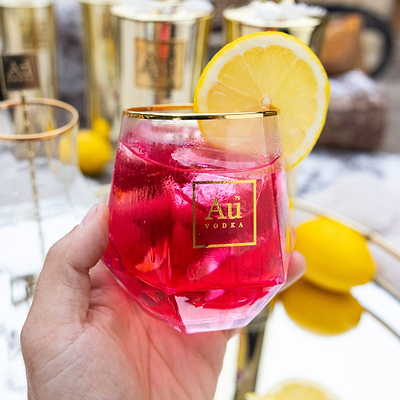 Person holding Diamond Cut Glass filled with, Pink Lemonade, and a lemon slice garnish. 