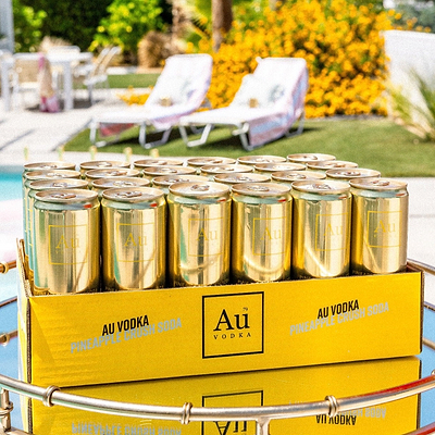 Case of Au Vodka USA Pineapple Crush cans on a tray by a pool
