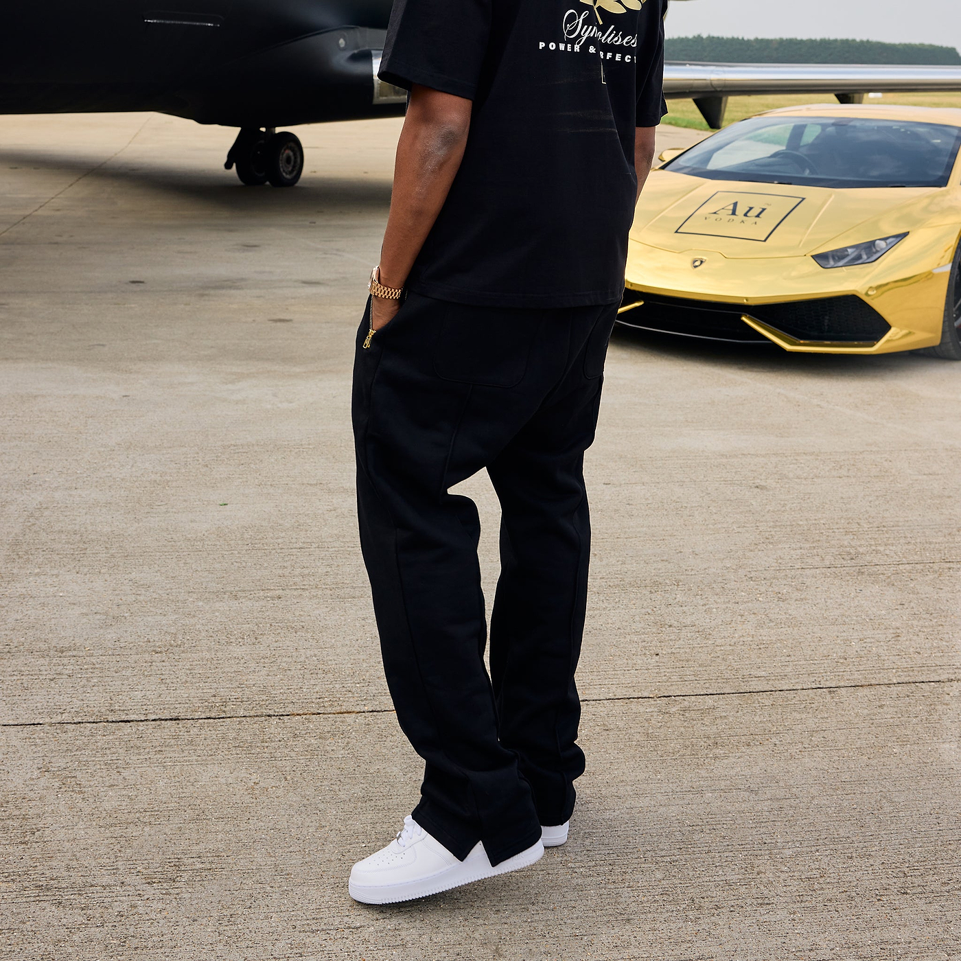Person in black outfit standing on a tarmac with a yellow sports