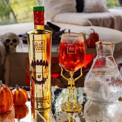 Gold bottle and glass with red liquid on a table with Halloween decorations.