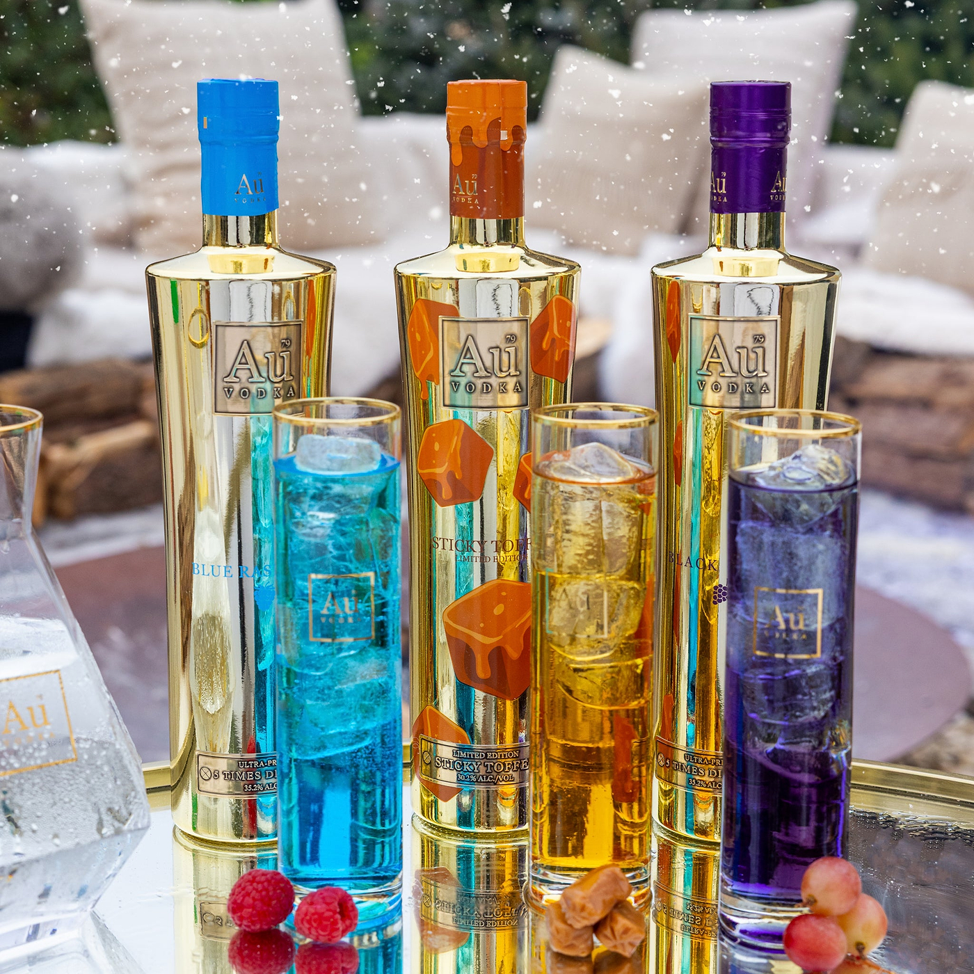 Three bottles of Au Vodka with colorful liquids and glasses on a reflective surface.