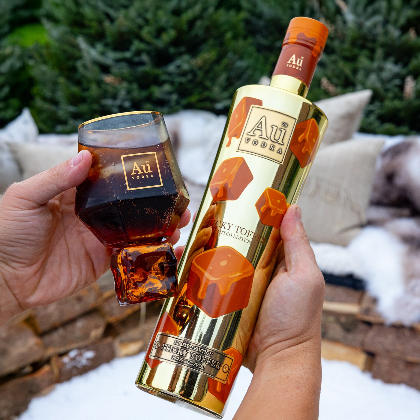 Person holding a bottle and glass of Au Vodka with decorative toffee elements outdoors.
