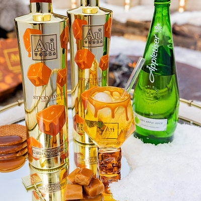 Two bottles of Vodka with orange candy pieces, a glass of cocktail, and a bottle of Appletiser on ice.