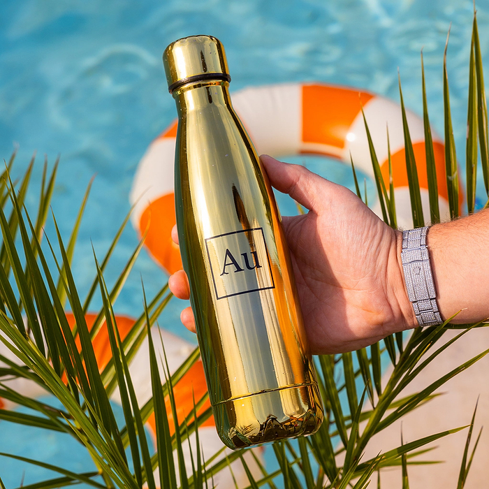 Hand holding a gold Au Vodka USA water bottle over a swimming pool with a life preserver