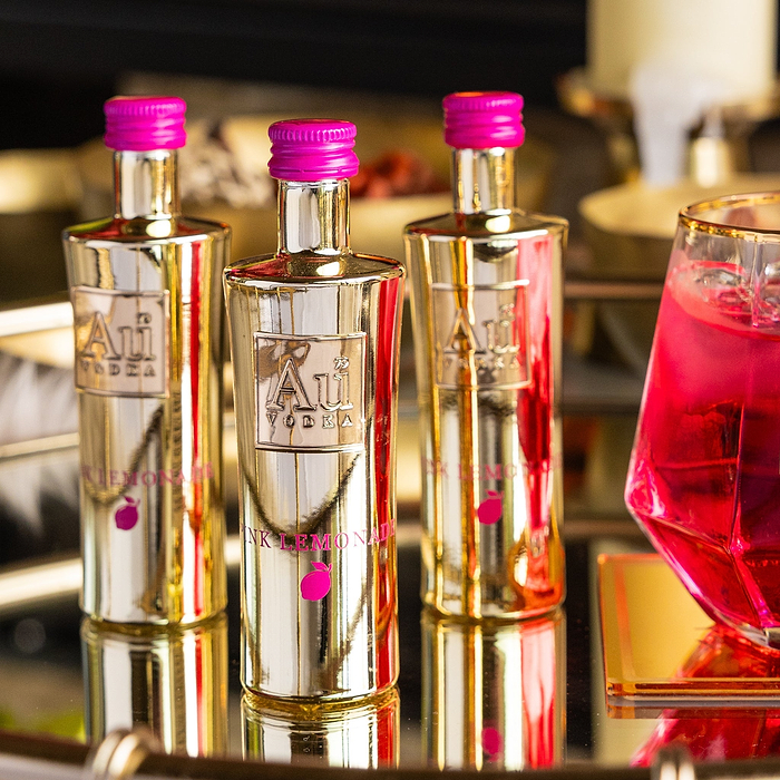 Three Bottles of Au Vodka Pink Lemonade on a reflective surface.