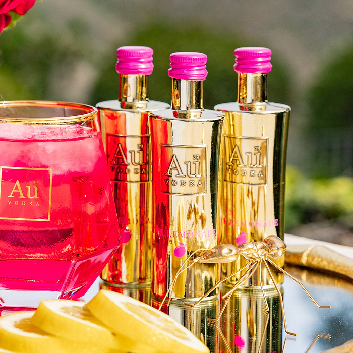 Three bottles of Au Vodka Pink Lemonade 50ml with a pink liquid and lemon slices on a reflective surface.