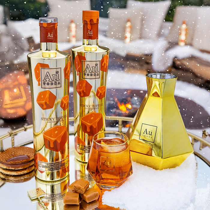 Two Bottles of Au Vodka Limited Edition Sticky Toffee. Au Vodka Glass with toffee liquid, on a reflective surface.