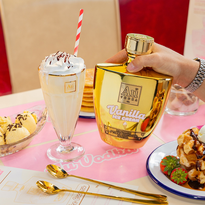 Person holding Au Vodka Bottle labeled 'Vanilla Ice Cream' with a sundae dessert and ice cream in the background.