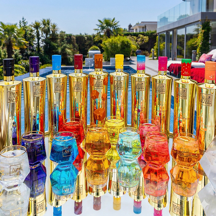 Au Vodka USA bottles and glasses in various colors on a reflective surface outdoors