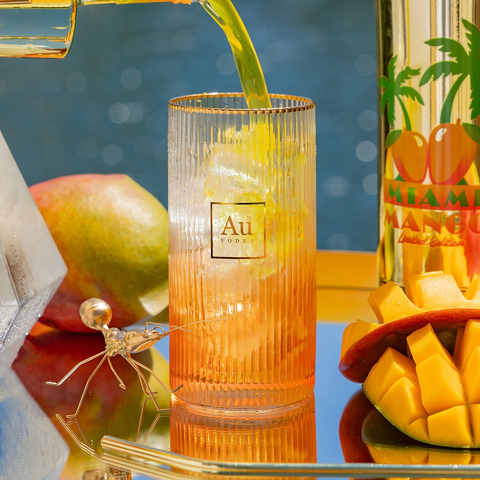 Au Vodka USA mango cocktail being poured, with mango fruit and Au Vodka bottle