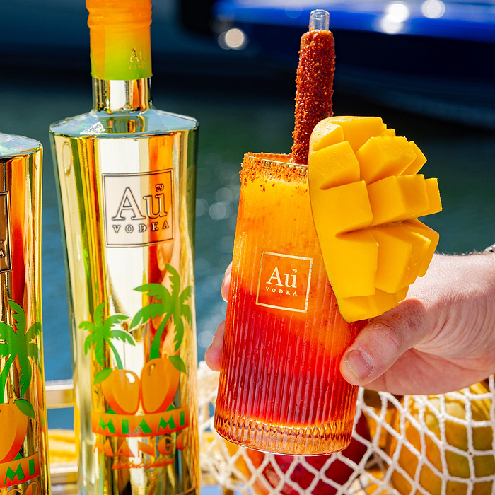 Hand holding an Au Vodka USA mango cocktail with a chili straw and mango garnish